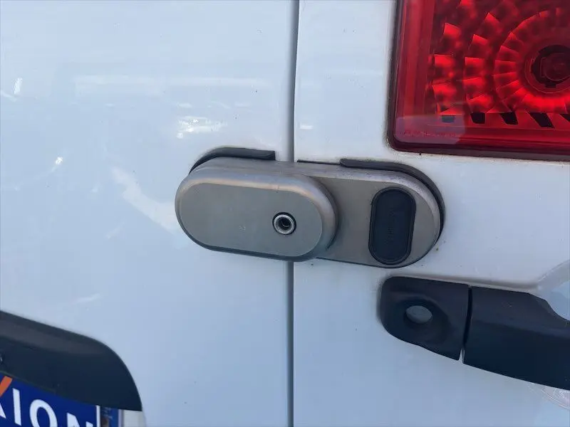 Gros plan sur la serrure antivol grise fixée sur la porte arrière blanche d’un Renault Master 2021, avec feu arrière rouge visible.