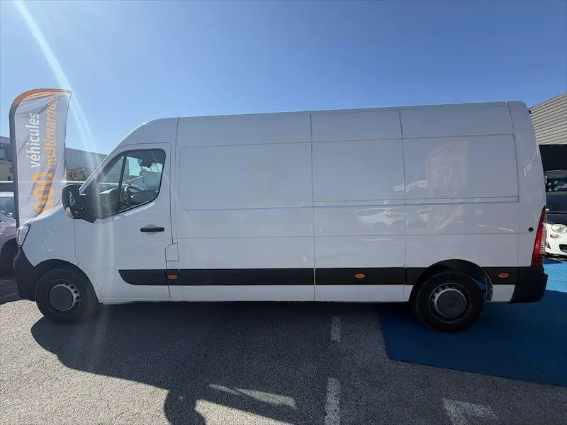 Profil côté gauche d’un utilitaire Renault Master blanc, grand volume, stationné en extérieur sous un ciel bleu.