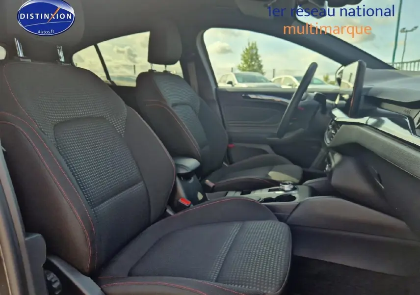 Intérieur avant de la Ford Focus 1.5 Ecoblue 115 ST-Line 2024, sièges noirs avec surpiqûres rouges et console centrale visible.