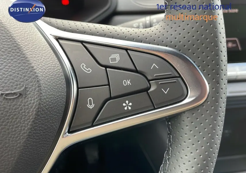 Gros plan sur les commandes multifonctions à gauche du volant perforé du Renault Captur rouge passion 2025.