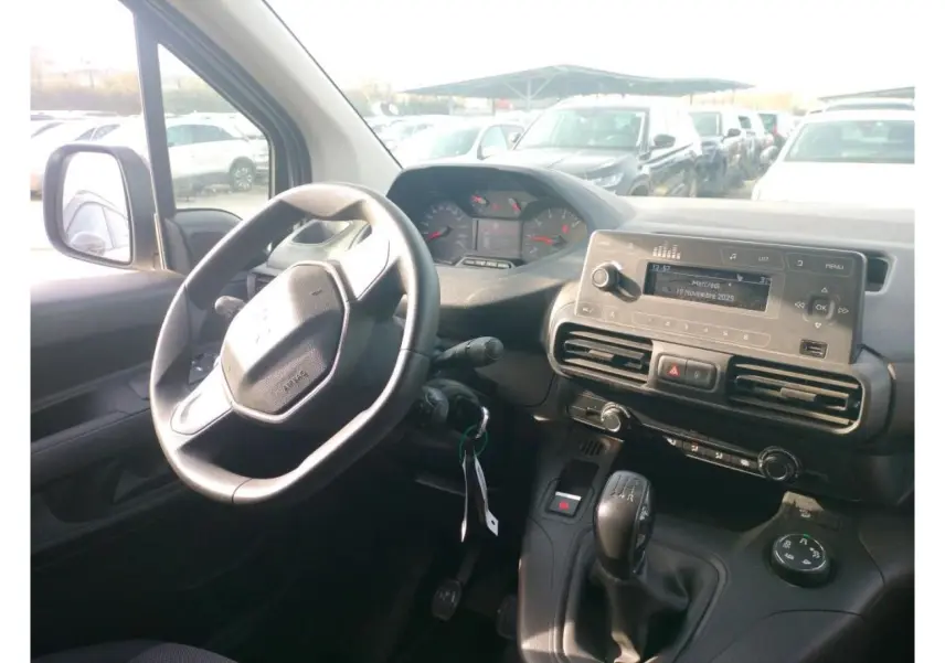 Vue de profil côté droit du Peugeot Partner blanc 2021 avec porte latérale coulissante ouverte sur un parking extérieur.