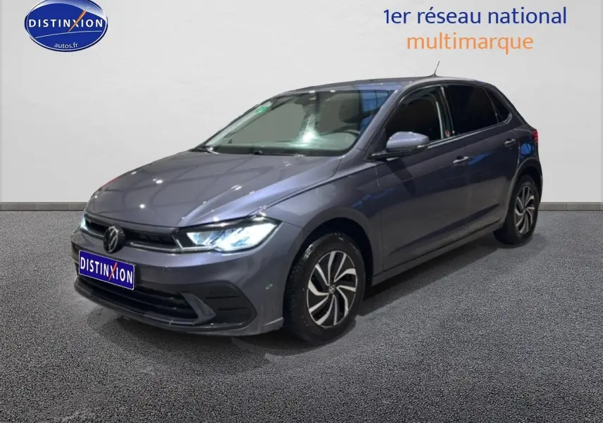 Volkswagen Polo gris cendre vue 3/4 avant droit avec phares allumés sur fond neutre intérieur.