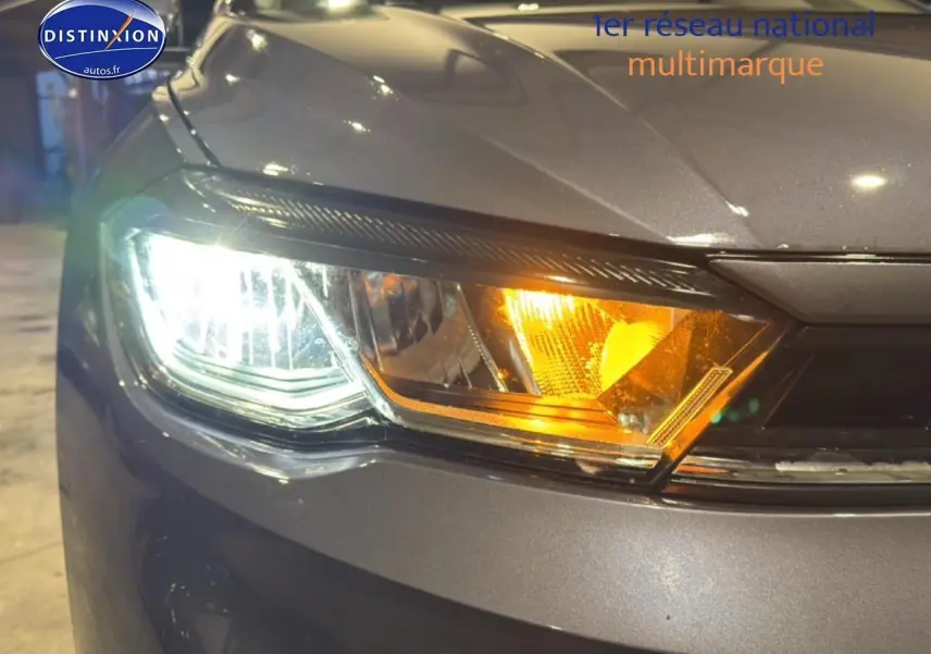 Gros plan sur le phare avant gauche allumé d'une Volkswagen Polo gris cendre avec clignotant orange visible.