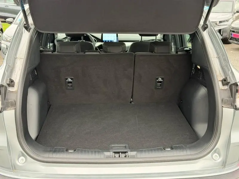 Vue arrière du coffre ouvert du Ford Kuga 2024 gris, montrant l'espace de chargement et les dossiers de sièges noirs.
