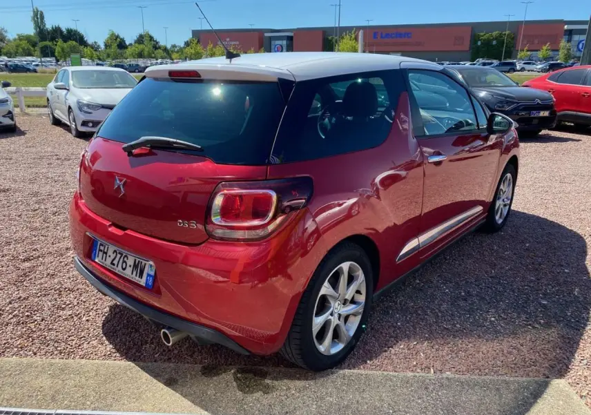 Vue 3/4 arrière droite d'une DS3 rouge à toit blanc avec jantes alliage et feux arrière distinctifs.