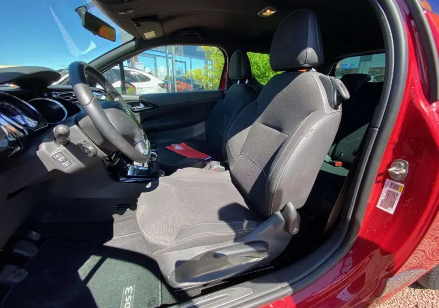 Vue intérieure côté conducteur d'une DS3 rouge avec sièges tissu gris et tableau de bord noir.