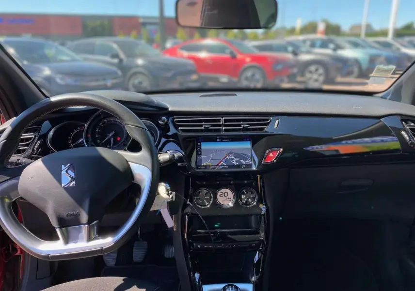 Vue intérieure avant du tableau de bord d'une DS3 rouge avec toit blanc, affichage tactile et volant noir.