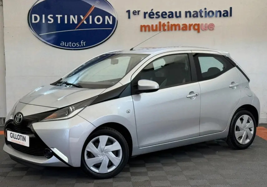 Toyota Aygo gris clair vue de profil côté gauche, soulignant son design compact et moderne en intérieur showroom.