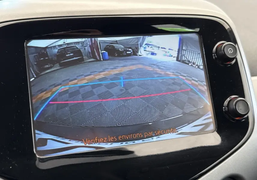Vue de l'écran de caméra de recul d'une Toyota Aygo gris clair, affichant les lignes de guidage et l'arrière du véhicule.