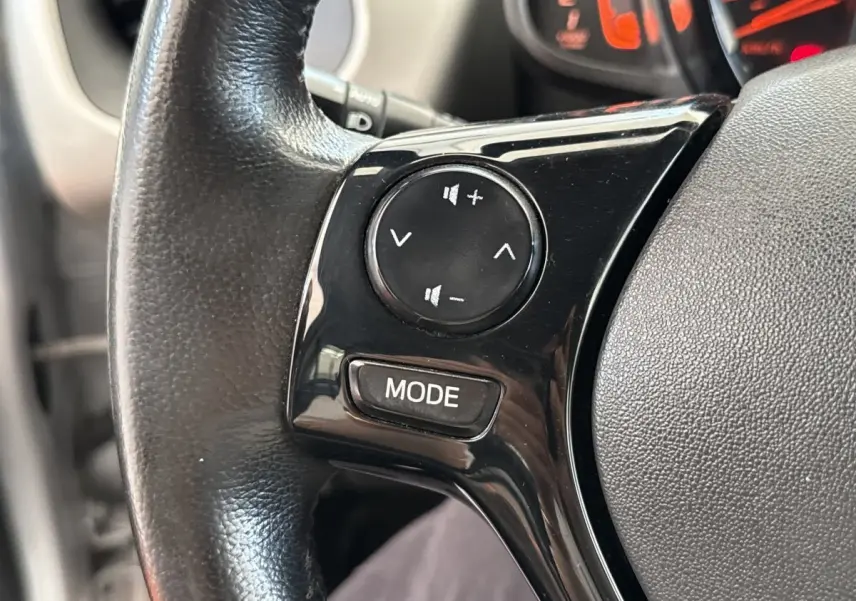 Gros plan sur le volant noir de la Toyota Aygo 2017, avec commandes audio intégrées et tableau de bord en arrière-plan.