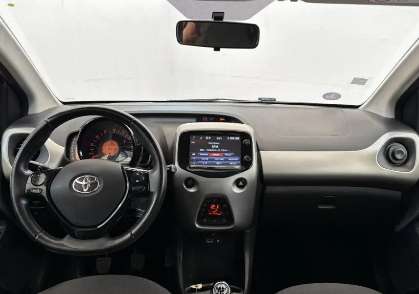 Vue intérieure frontale du tableau de bord gris clair et noir de la Toyota Aygo 2017 avec volant multifonction et écran tactile central.