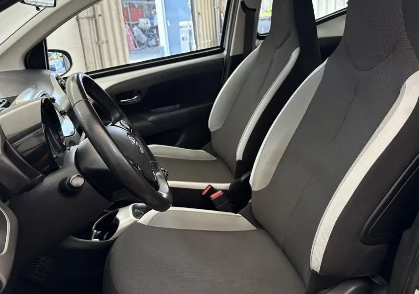 Vue intérieure côté conducteur de la Toyota Aygo 2017, sièges tissu gris clair et noir avec volant réglable.