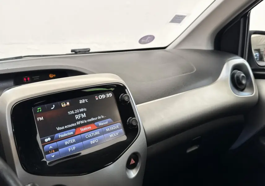 Vue intérieure du tableau de bord de la Toyota Aygo gris clair, avec écran tactile central affichant la radio FM.