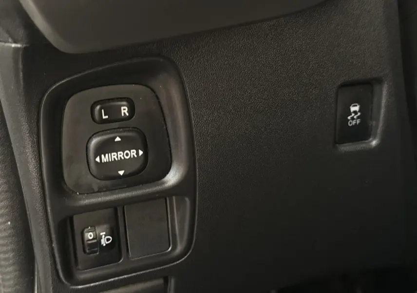 Gros plan sur les commandes de réglage des rétroviseurs et bouton antipatinage dans l'habitacle d'une Toyota Aygo gris clair.