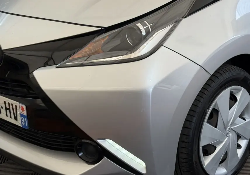 Gros plan sur l'avant droit gris clair de la Toyota Aygo 2017, mettant en valeur le phare et la roue.