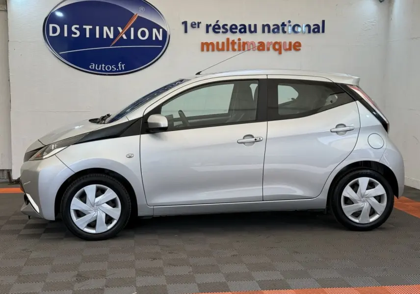 Profil droit d'une Toyota Aygo gris clair 2017 avec jantes argentées et bande noire distinctive sur l'aile avant.