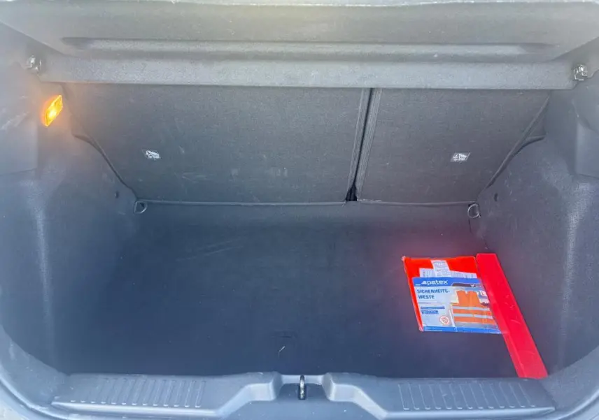 Coffre ouvert d'une Citroën C3 gris foncé 2025, avec gilet de sécurité orange et triangle de signalisation rouge à droite.
