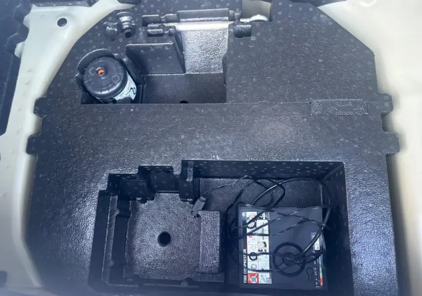 Rangement sous le coffre d'une Citroën C3 gris foncé 2025, montrant le compresseur de pneu et espace de rangement en mousse noire.
