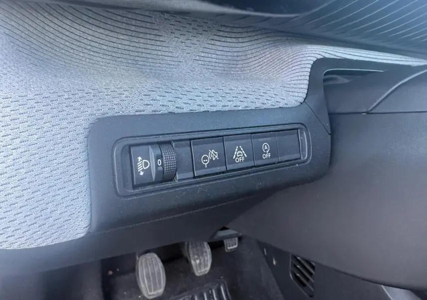 Détail des commandes situées à gauche sous le tableau de bord du Citroën C3 gris foncé, avec pédales manuelles visibles.