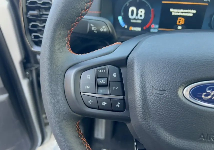 Gros plan sur le volant cuir noir avec surpiqûres orange du Ford Ranger Wildtrak 2026, boutons multifonctions visibles.