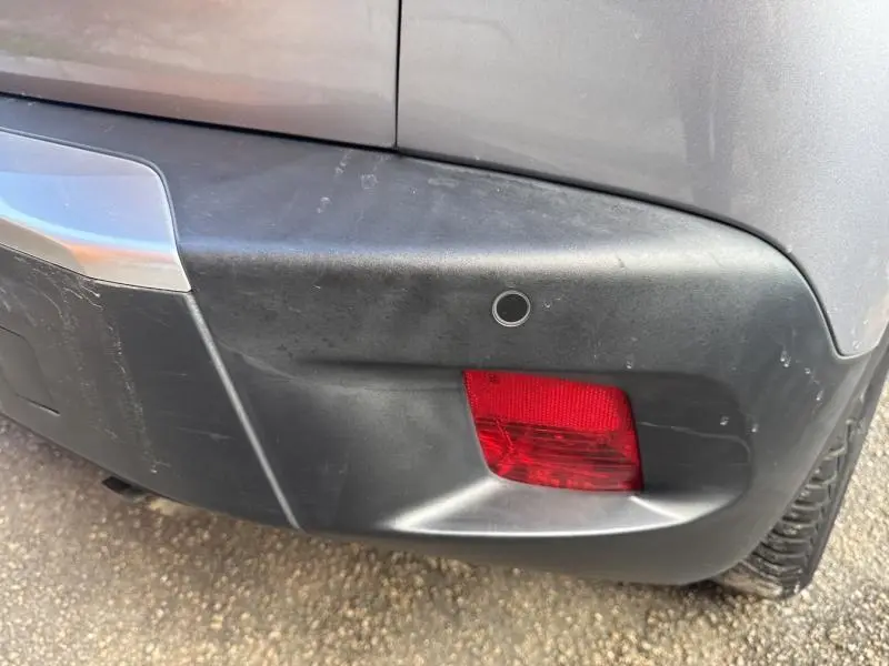Gros plan sur le pare-chocs arrière droit gris Artense du Peugeot 2008 avec feu antibrouillard rouge et capteur de recul.