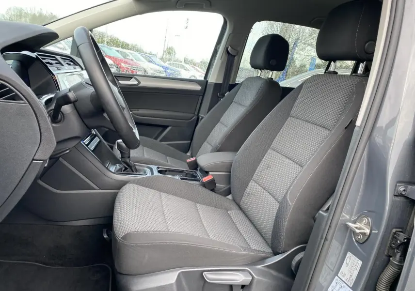 Vue intérieure côté conducteur du Volkswagen Touran gris dauphin, montrant les sièges avant et le volant multifonction.