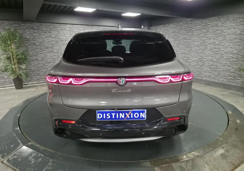 Vue arrière d'une Alfa Romeo Tonale gris métallisé avec feux LED allumés et logo central dans un showroom.