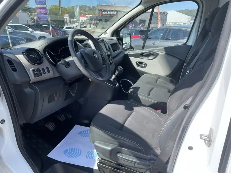 Vue intérieure côté conducteur du Renault Trafic Fourgon blanc 2017, montrant le volant, la boîte manuelle et les sièges tissu noirs.