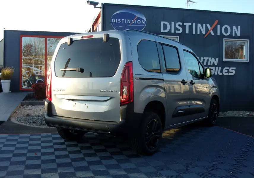 Vue 3/4 arrière droite d’un Citroën Berlingo gris Artense 2025, avec vitres teintées et jantes noires, stationné devant un bâtiment.