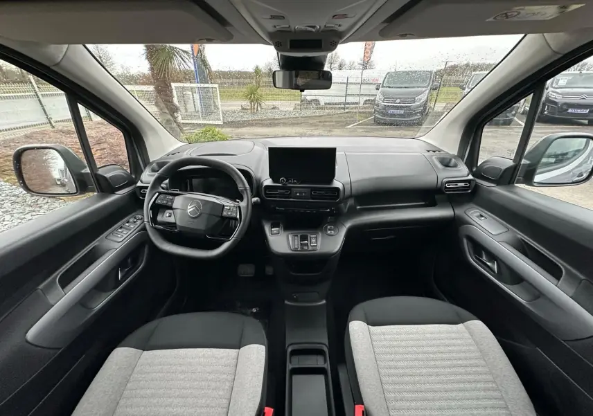 Vue intérieure avant du Citroën Berlingo 2025, tableau de bord noir avec écran central et sièges bicolores gris et noir.