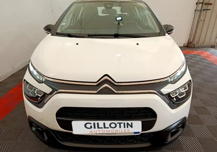 Vue frontale d'une Citroën C3 blanche avec calandre noire et feux LED distinctifs, stationnée en intérieur.