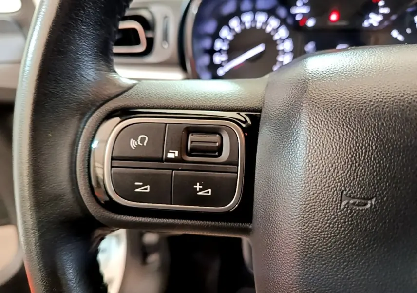 Gros plan sur le volant cuir noir de la Citroën C3 2021 avec commandes multifonctions et tableau de bord lumineux flou.