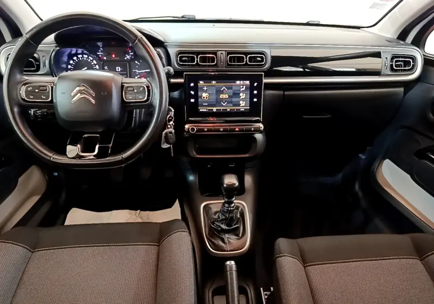 Vue intérieure avant du tableau de bord d'une Citroën C3 blanche, volant cuir multifonctions et écran tactile central allumé.