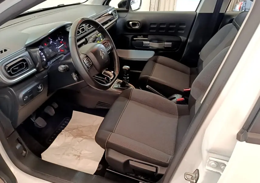 Vue intérieure côté conducteur de la Citroën C3 blanche 2021, volant cuir multifonctions et sièges tissu gris.