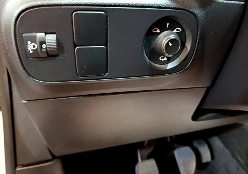 Détail du panneau de commandes côté conducteur avec réglage des phares et commande des rétroviseurs dans une Citroën C3 blanche.