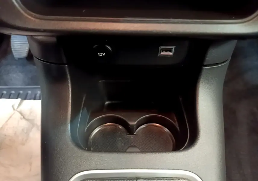 Gros plan sur la console centrale noire de la Citroën C3, montrant prise 12V, port USB et porte-gobelets.