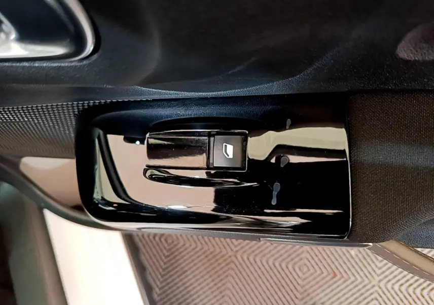 Gros plan sur le bouton de commande de la vitre électrique côté conducteur dans l'habitacle noir d'une Citroën C3 blanche.