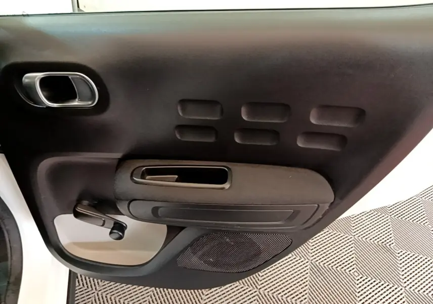 Gros plan sur la porte avant gauche noire avec poignée argentée et manivelle de vitre d'une Citroën C3 blanche.