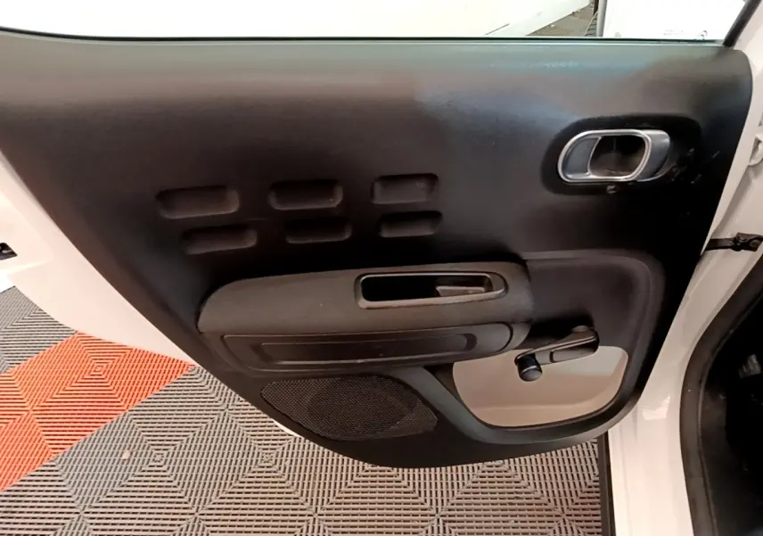 Vue intérieure de la porte avant gauche blanche d'une Citroën C3 2021 avec poignée et commande de vitre manuelle.