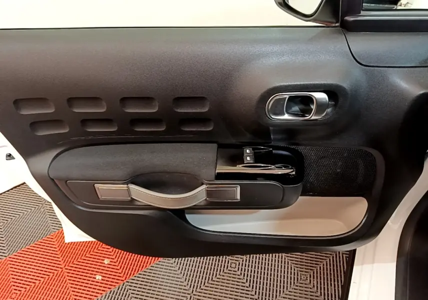 Vue intérieure de la porte avant gauche blanche de la Citroën C3 avec poignée noire et commandes électriques des vitres.