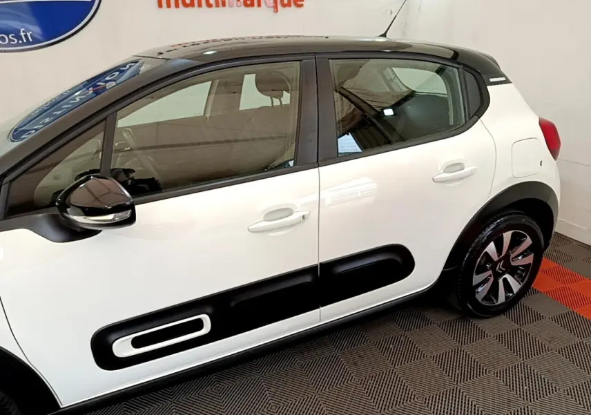 Vue de profil côté droit d'une Citroën C3 blanche avec toit noir et protections latérales noires distinctives.