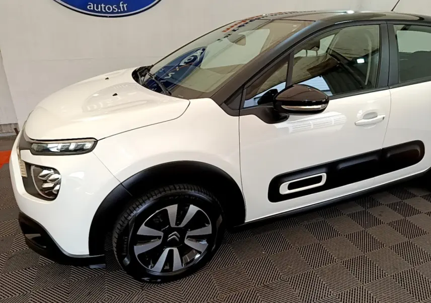 Vue 3/4 avant droit d'une Citroën C3 blanche 2021 avec protections latérales noires et jantes bicolores.