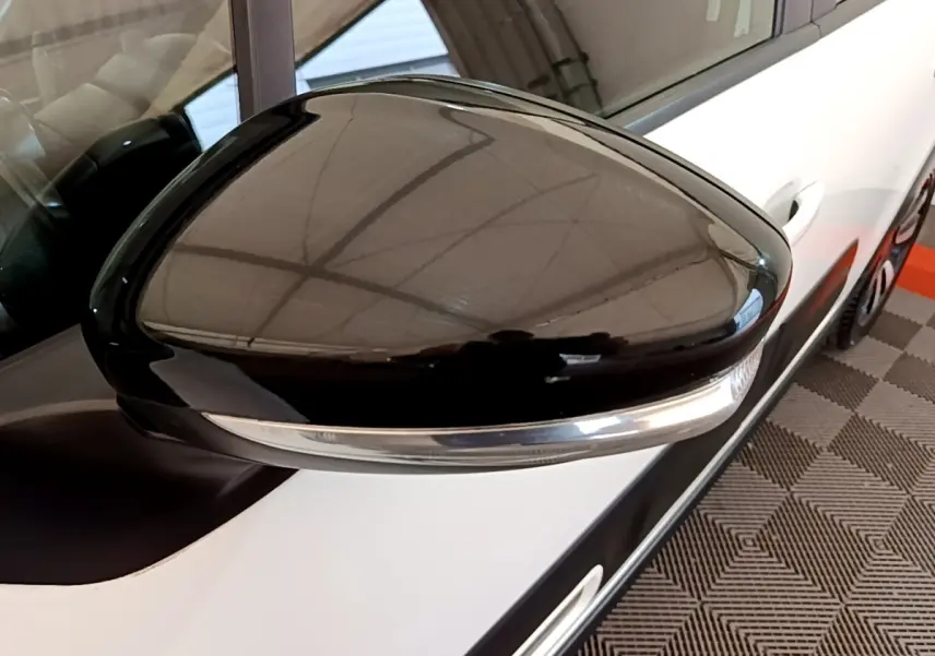 Gros plan sur le rétroviseur noir côté conducteur d'une Citroën C3 blanche, vue partielle du flanc avant droit.