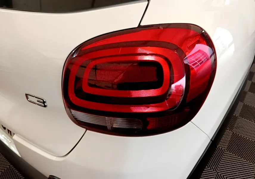 Gros plan sur le feu arrière droit rouge et le logo C3 d'une Citroën C3 blanche vue de l'arrière.