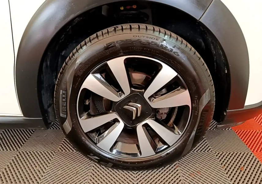Gros plan sur la roue avant droite d'une Citroën C3 blanche, mettant en valeur la jante noire et argentée au logo Citroën.