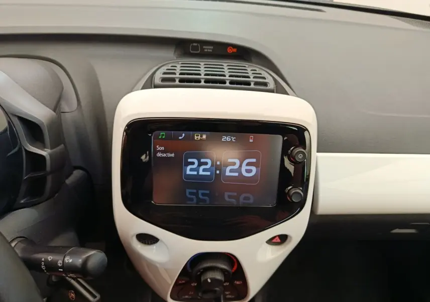 Vue rapprochée du tableau de bord blanc de la Toyota Aygo 2016 avec écran tactile affichant l'heure et la température.