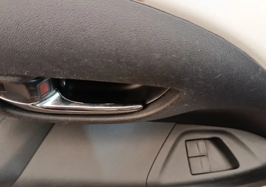 Poignée intérieure chromée et commandes des vitres électriques sur la porte côté conducteur d'une Toyota Aygo blanche.