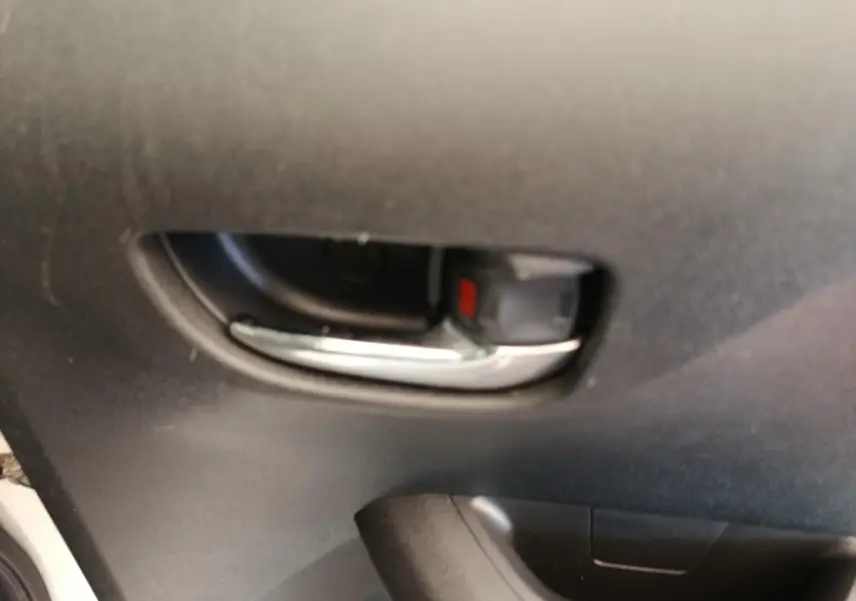 Poignée intérieure de porte avant gauche d'une Toyota Aygo blanche, finition 2016, avec insert chromé et bouton de verrouillage rouge.