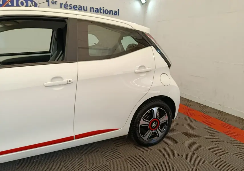 Vue côté droit arrière d'une Toyota Aygo blanche 2016 avec jantes noires et détails rouges sur la carrosserie.