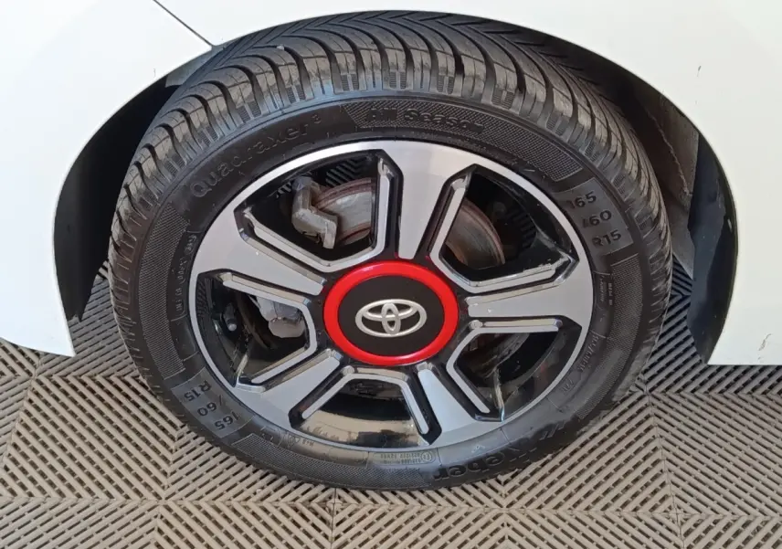 Gros plan sur la roue avant droite d'une Toyota Aygo blanche, avec jante noire et rouge au centre.